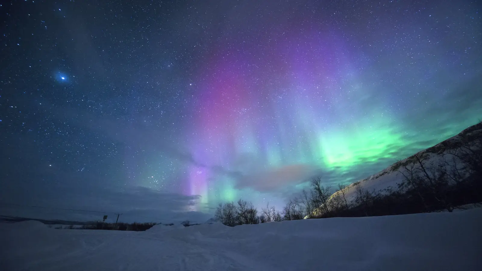 Aurores boréales vertes au-dessus de montagnes enneigées la nuit