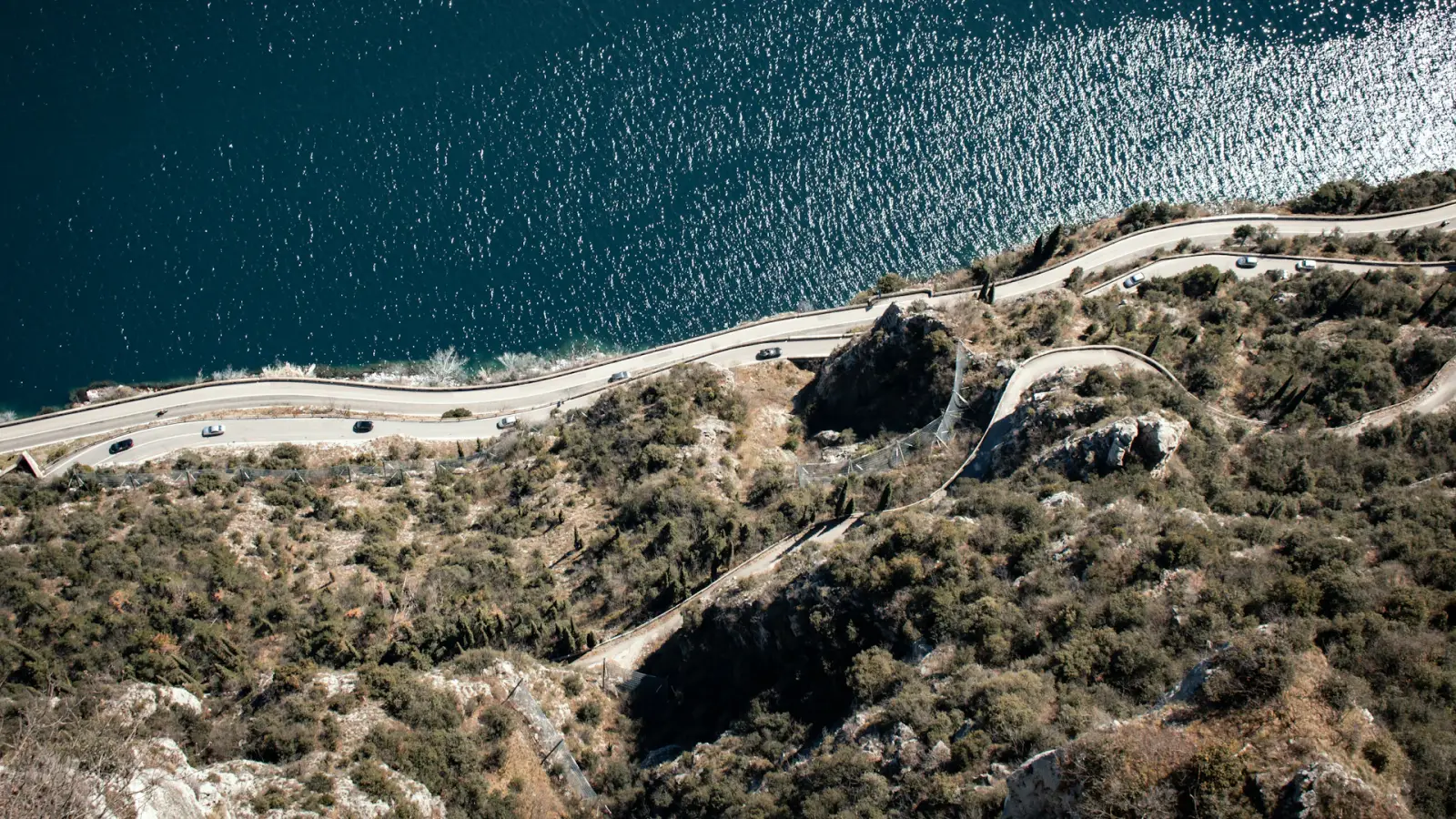 Route sinueuse longeant un lac bleu, vue aérienne d'un road trip en Europe
