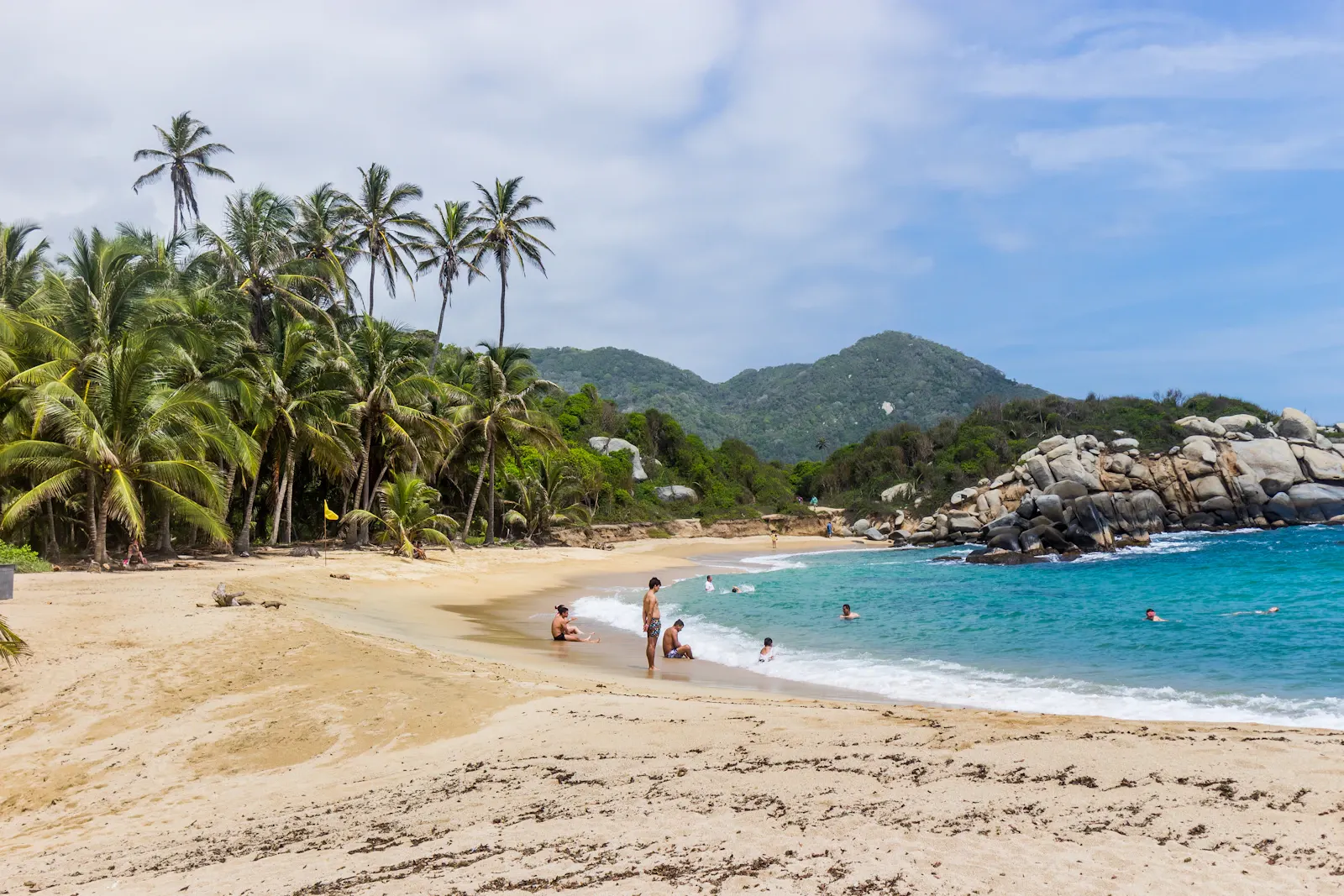 Plage du parc Tayrona bordée de palmiers, baigneurs dans l'eau turquoise